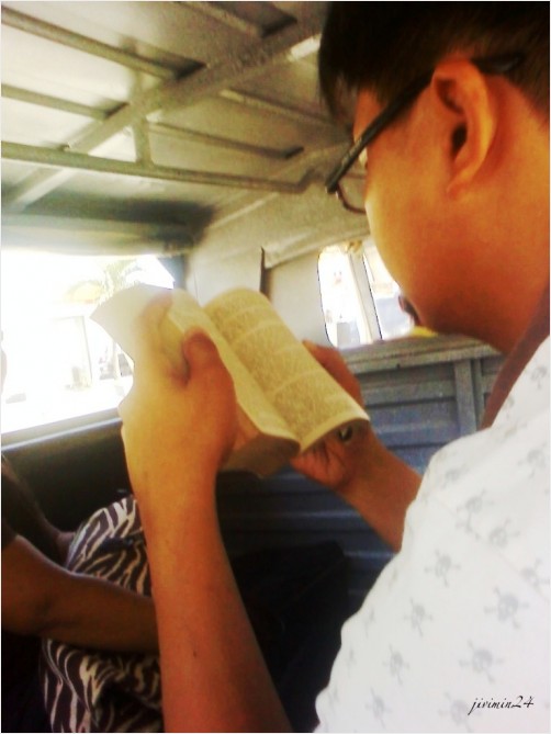 A guy reading a book in a jeepney/car